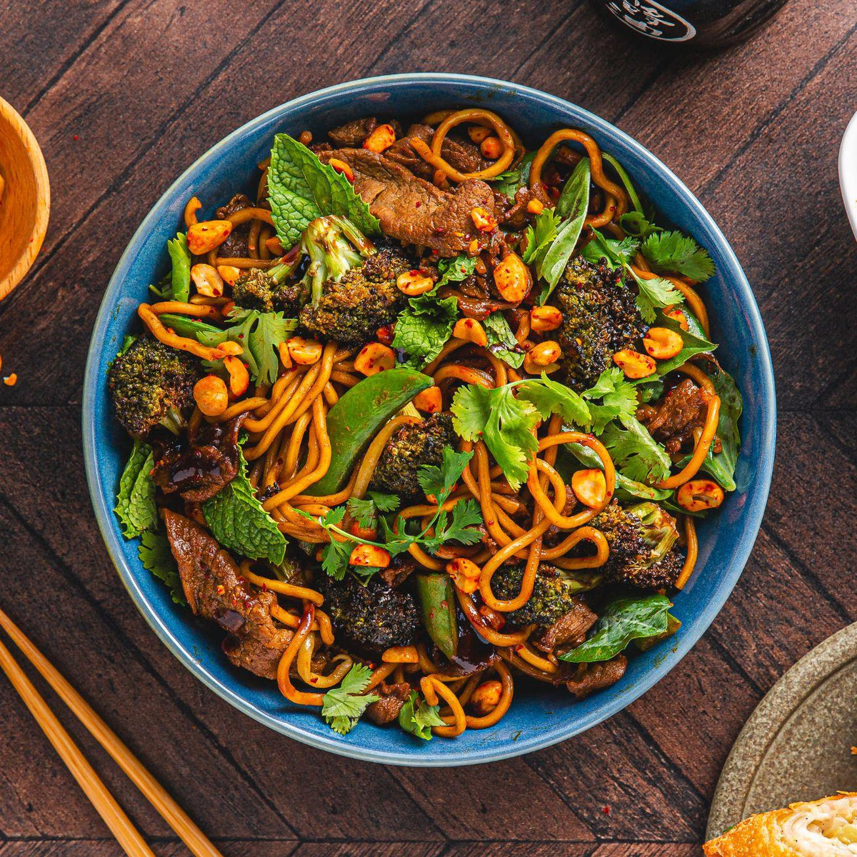 A bowl of stir-fried noodles with vegetables, beef, peanuts, and fresh herbs.