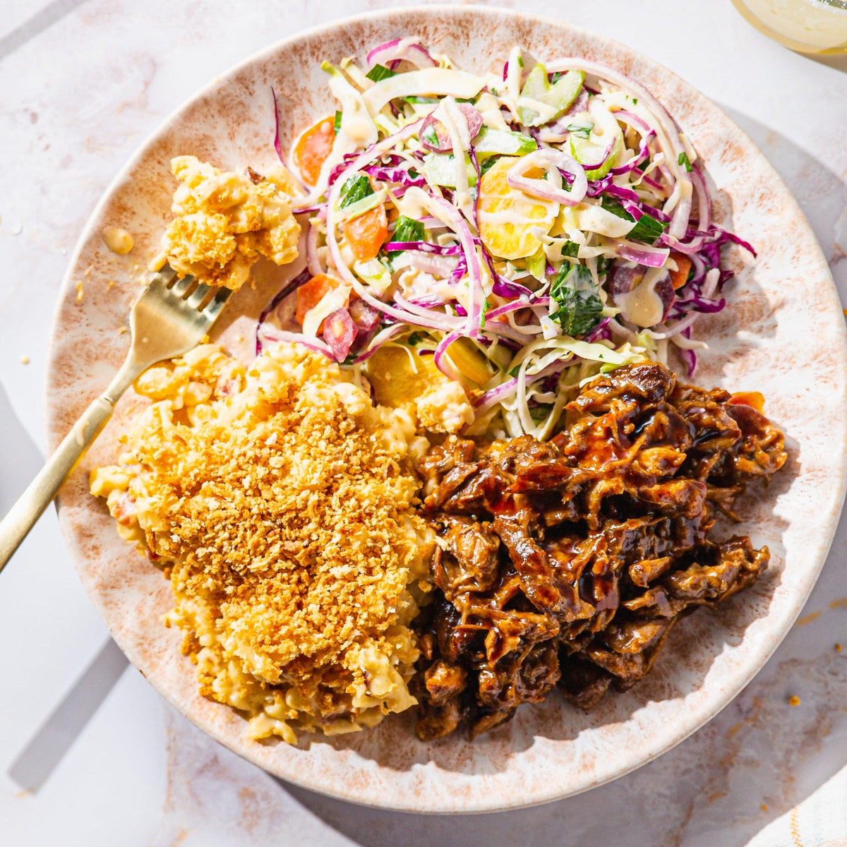 Plate with mac 'n' cheese, barbecue pulled pork, and a fresh vegetable salad.