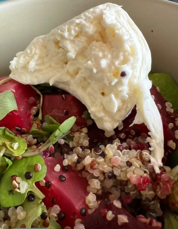 A salad bowl with quinoa, beet slices, greens, and a dollop of soft cheese.